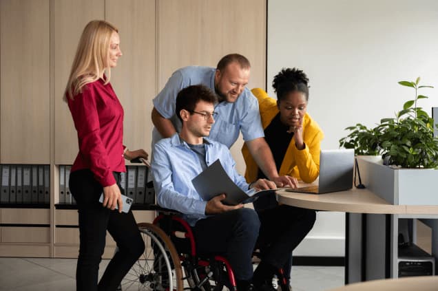 Team of professionals collaborating at a desk, including a man using a wheelchair
