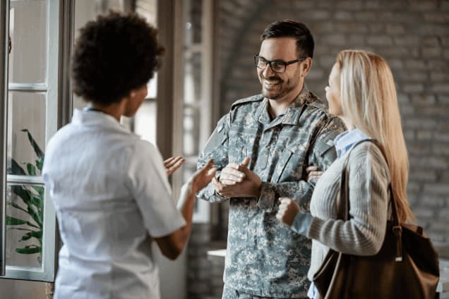 A smiling male soldier in uniform and his partner speaking with a female medical professional.