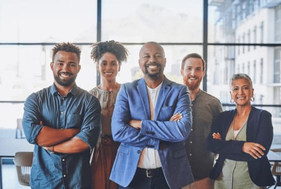 Five diverse professionals standing together in an office, smiling with arms crossed